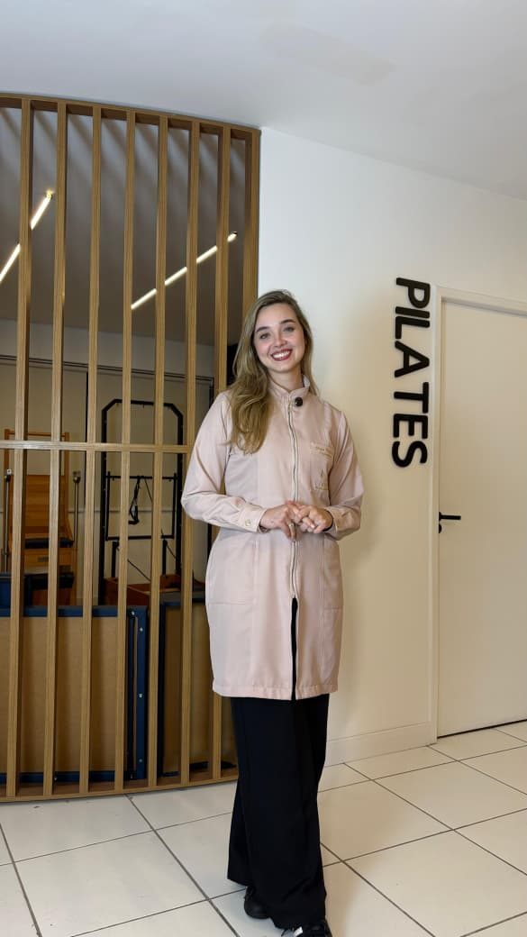 Bruna Baptista em pé, sorrindo, em frente à sala de Pilates